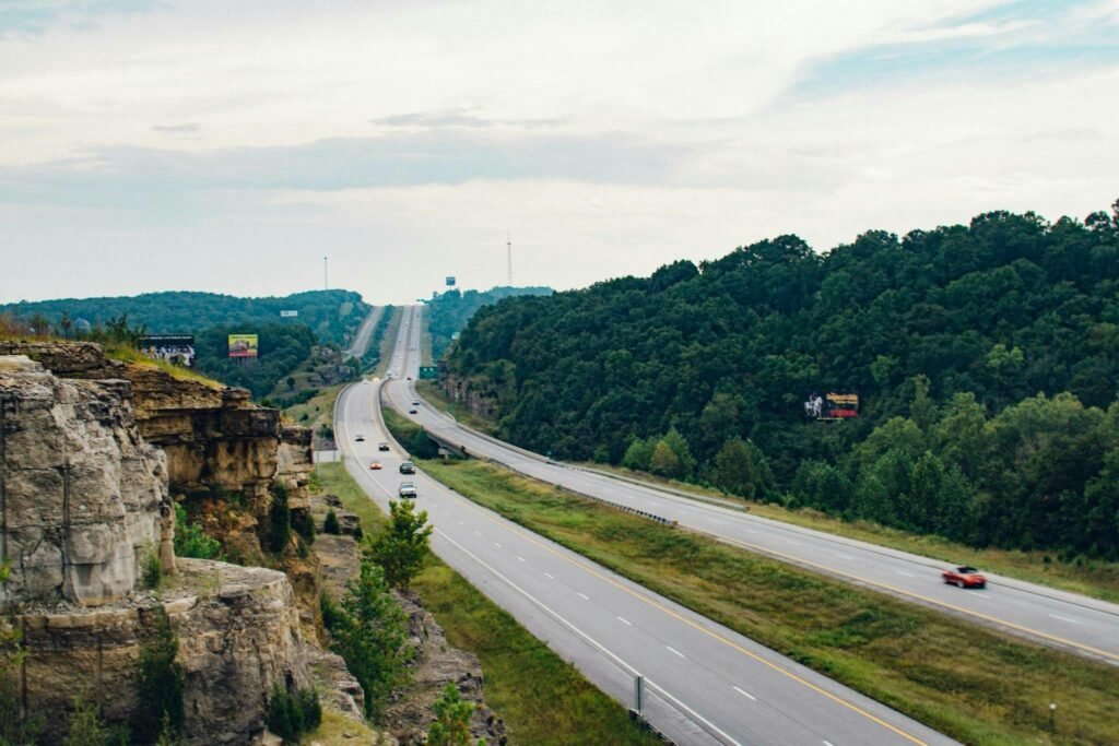 Aerial view of a highway cutting through lush green landscapes with cliffs and signs visible.